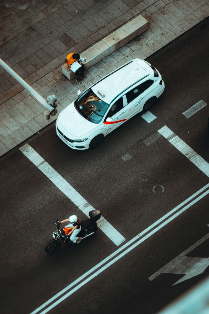 a white car driving down a street next to a motorcycle
